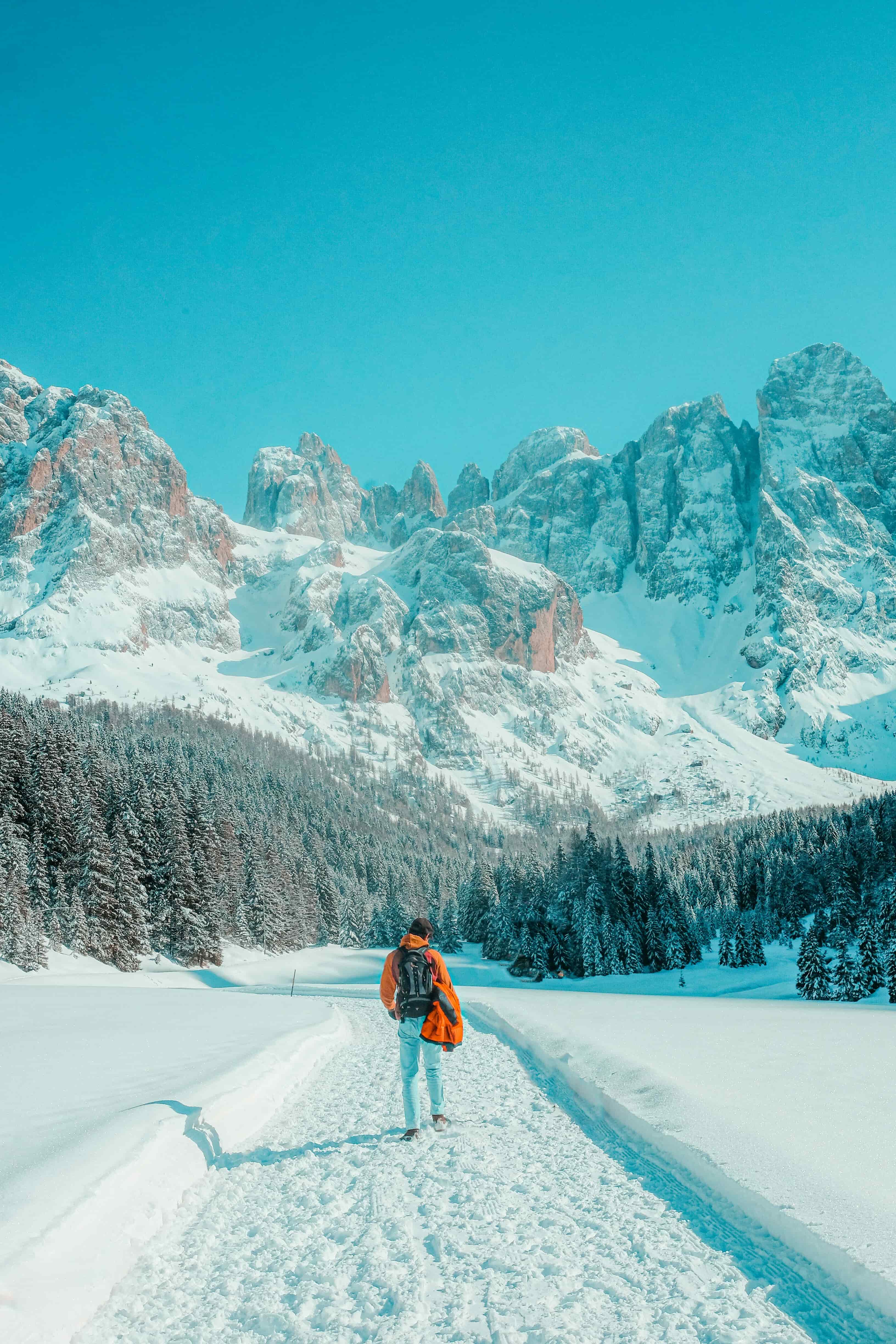 Person hiking through snow toward dramatic alpine mountain peaks